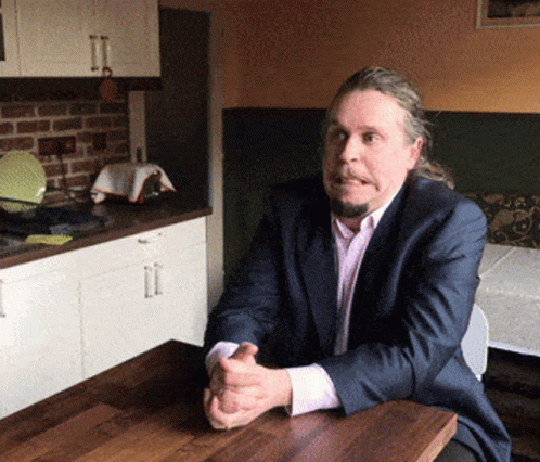 A Man Sitting At A Table With His Hands Folded GIF