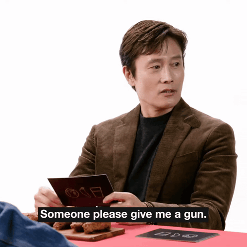 A Man Sitting At A Table With Someone Please Give Me A Gun Written On The Bottom GIF