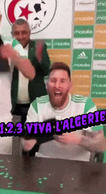 A Man Sitting At A Table With The Words 123 Viva L' Algerie GIF
