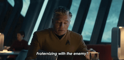 A Man Sitting At A Table With The Words " Fraternizing With The Enemy " Below Him GIF
