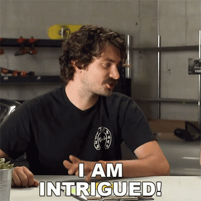 A Man Sitting At A Table With The Words I Am Intrigued GIF