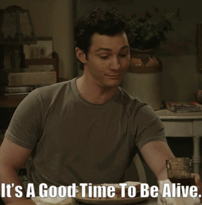 A Man Sitting At A Table With The Words It 'S A Good Time To Be Alive On The Bottom GIF