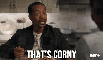 A Man Sitting At A Table With The Words That 'S Corny Written Below Him GIF