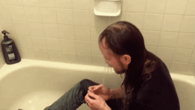 A Man Sitting In A Bathtub With A Dove Soap Dispenser On The Wall Behind Him GIF