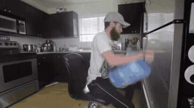 A Man Sitting In A Chair In A Kitchen With A Microwave That Says " Powder " On It GIF