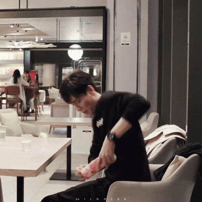 A Man Sitting In A Chair In Front Of A Sign That Says Milklab GIF