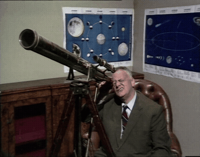 A Man Sitting In A Chair Looking Through A Telescope With Posters On The Wall Behind Him GIF