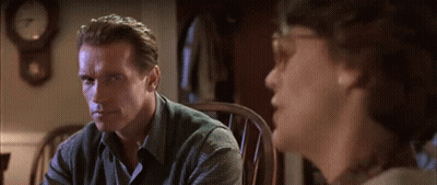 A Man Sitting In A Chair Talking To Another Man With A Clock In The Background GIF