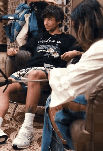 A Man Sitting In A Chair Wearing A Neighborhood Sweatshirt GIF