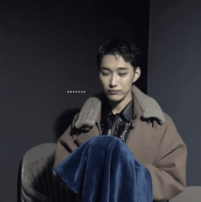 A Man Sitting In A Chair With A Blue Blanket Around His Knee GIF