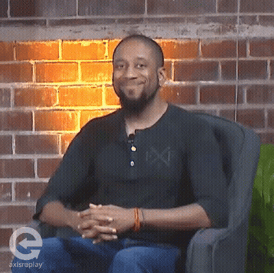 A Man Sitting In A Chair With A Brick Wall Behind Him And A Logo For Axisreplay On The Bottom GIF