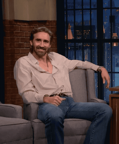 A Man Sitting In A Chair With His Arm Resting On The Arm Rest GIF