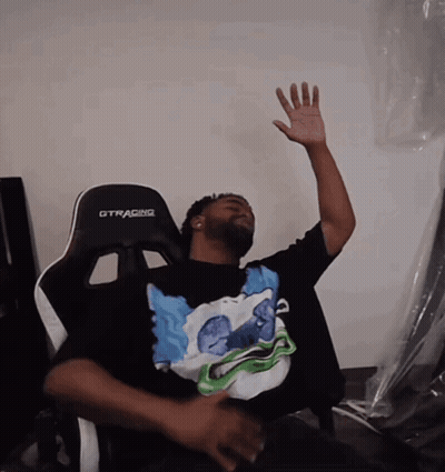 A Man Sitting In A Gtracing Chair With His Hand Up In The Air GIF