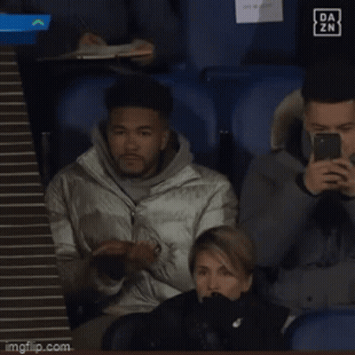 A Man Sitting In A Stadium Looking At His Phone With A Da Zn Logo In The Background GIF