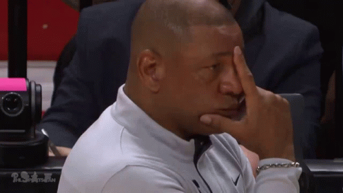 A Man Sitting In A Stadium With His Hand On His Face GIF