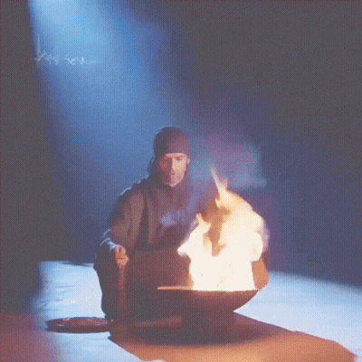 A Man Sitting In Front Of A Bowl Of Fire With Smoke Coming Out Of It GIF