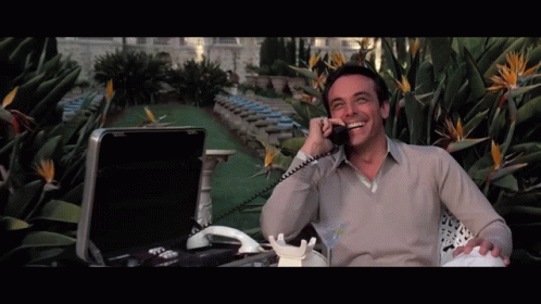 A Man Sitting In Front Of A Briefcase Talking On A Telephone GIF