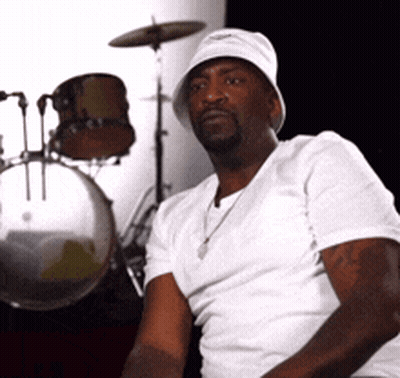 A Man Sitting In Front Of A Drum Set Wearing A Hat GIF