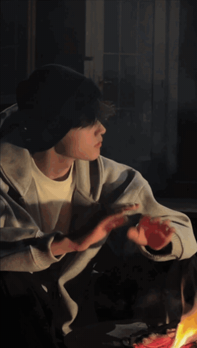 A Man Sitting In Front Of A Fire With His Hand Outstretched GIF