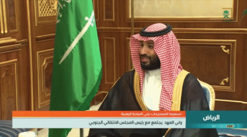 A Man Sitting In Front Of A Green And White Flag With The Words " الرياض " On The Bottom GIF