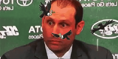 A Man Sitting In Front Of A Green Background That Says At GIF