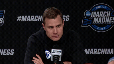A Man Sitting In Front Of A March Madness Banner GIF