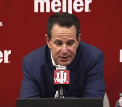 A Man Sitting In Front Of A Meijer Sign Talking Into A Microphone GIF