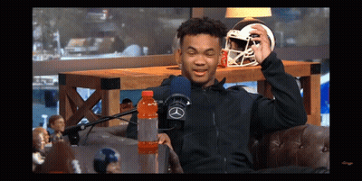 A Man Sitting In Front Of A Microphone Holding A Football Helmet And A Gatorade Bottle GIF