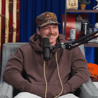 A Man Sitting In Front Of A Microphone Wearing A Hat That Says ' Abercrombie & Fitch ' On It GIF