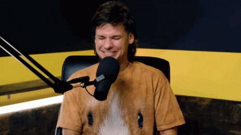 A Man Sitting In Front Of A Microphone Wearing A Shirt With A Horse On It GIF