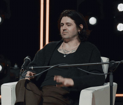A Man Sitting In Front Of A Microphone With A Tattoo On His Arm GIF