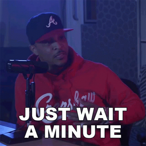 A Man Sitting In Front Of A Microphone With The Words Just Wait A Minute Written Below Him GIF