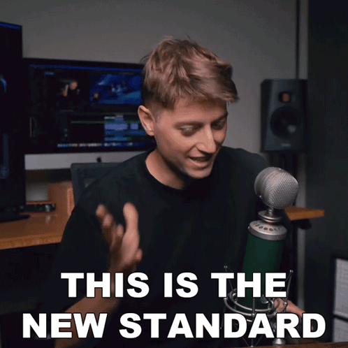 A Man Sitting In Front Of A Microphone With The Words This Is The New Standard Above Him GIF