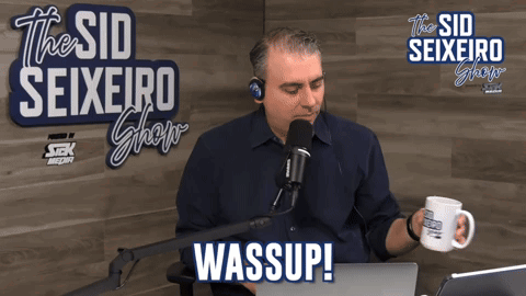A Man Sitting In Front Of A Microphone With The Words Wassup On The Bottom Right GIF