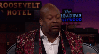 A Man Sitting In Front Of A Roosevelt Hotel Sign With His Hands In The Air GIF