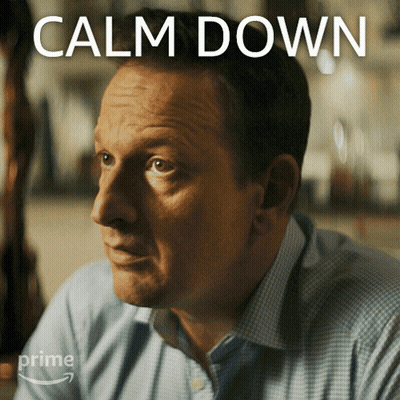 A Man Sitting In Front Of A Sign That Says " Calm Down " GIF