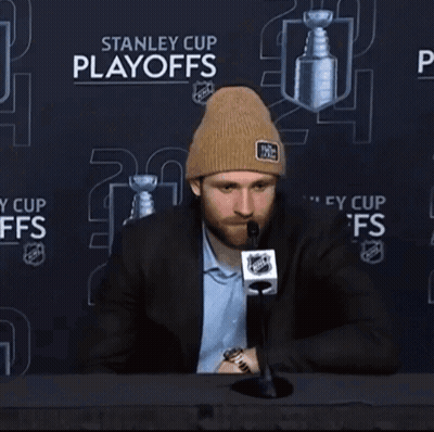 A Man Sitting In Front Of A Stanley Cup Playoffs Advertisement GIF