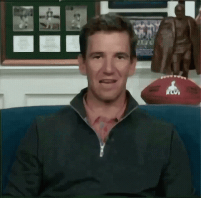 A Man Sitting In Front Of A Statue Of A Man And A Football GIF