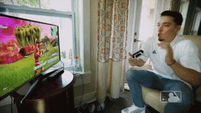 A Man Sitting In Front Of A Television With A Mlb Logo GIF