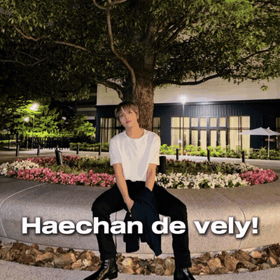 A Man Sitting In Front Of A Tree With The Words Haechan De Vely Written Below Him GIF
