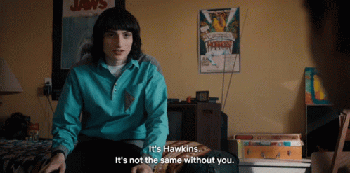 A Man Sitting On A Bed With A Poster On The Wall That Says Jaws GIF