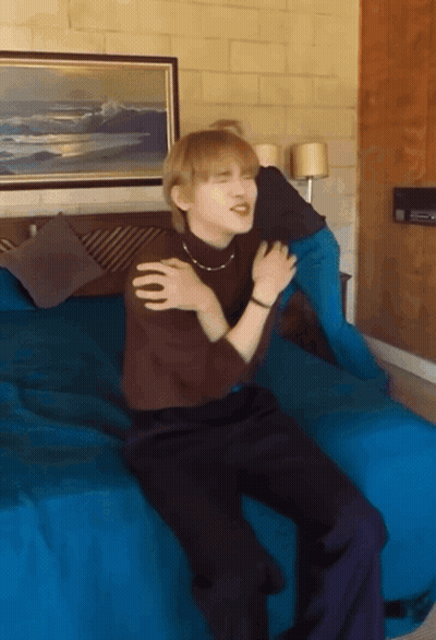 A Man Sitting On A Bed With His Arms Around His Shoulder GIF