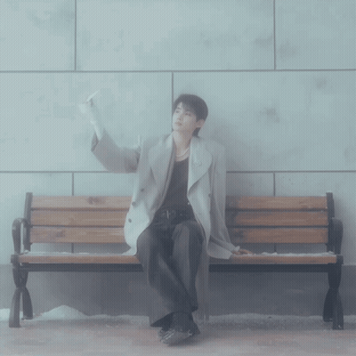 A Man Sitting On A Bench With His Hand Up GIF