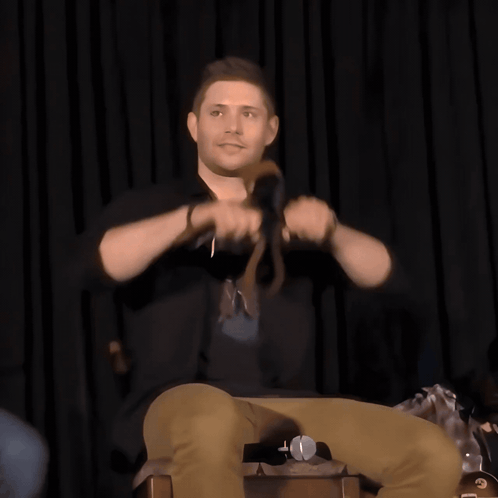 A Man Sitting On A Chair Holding A Microphone GIF