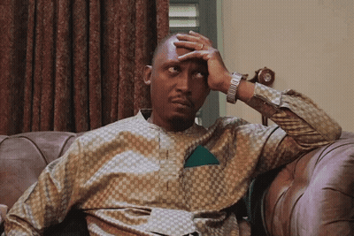 A Man Sitting On A Couch Covering His Face With His Hand GIF