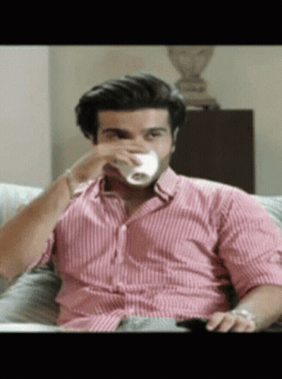 A Man Sitting On A Couch Drinking From A Cup GIF