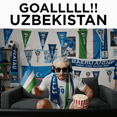 A Man Sitting On A Couch Holding A Bag Of Popcorn And Wearing A Scarf That Says Ufa GIF