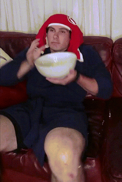 A Man Sitting On A Couch Holding A Bowl Of Soup GIF