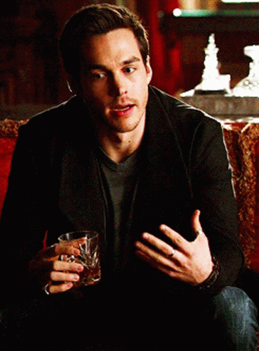 A Man Sitting On A Couch Holding A Glass Of Alcohol GIF