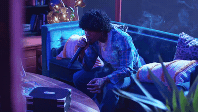 A Man Sitting On A Couch Holding A Microphone GIF